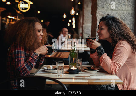 Vista laterale ritratto di due giovani donne di parlare e di bere il caffè in un bar. Amici di sesso femminile in un ristorante. Foto Stock