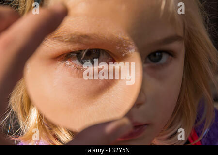 Close-up ritratto di una bella ragazza giovane guardando attraverso la lente di ingrandimento Foto Stock