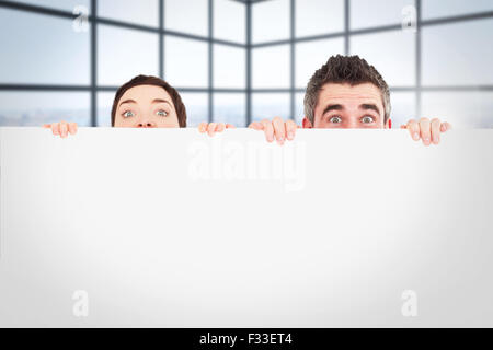 Immagine composita di un uomo e di una donna di nascondersi dietro un pannello bianco con camera per spazio di copia Foto Stock