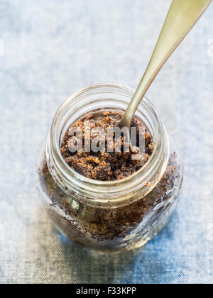 In casa per il viso e per il corpo tutto organico naturale macchia di caffè (peeling) in un vasetto di vetro. Cucchiaio posto all'interno. Orientamento verticale. Foto Stock