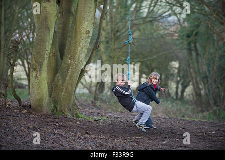 Bambini che giocano su una corda swing in foresta NORFOLK REGNO UNITO Foto Stock