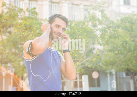 Bello atleta sorridente e mettendo nelle cuffie Foto Stock
