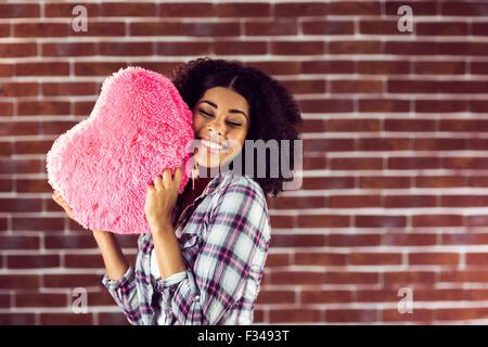 Attraente giovane donna cuddling con cuore-cuscino sagomato Foto Stock