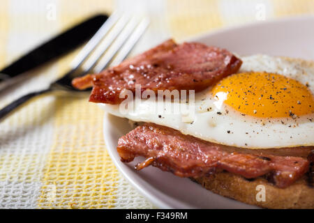 Close-up di uovo fritto con un pizzico di pepe e pancetta fritta su fette di pane integrale Foto Stock