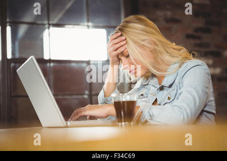 Oberati di lavoro bionda seduta e utilizzo di computer portatile Foto Stock