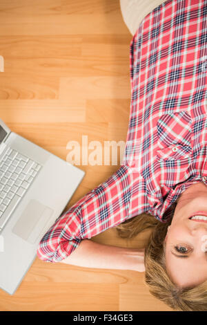 Donna sorridente sdraiato sul pavimento accanto al laptop Foto Stock