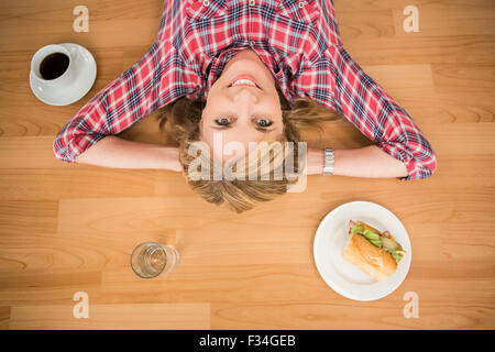 Donna sorridente giacente sul piano circondato da cibo e bevande Foto Stock