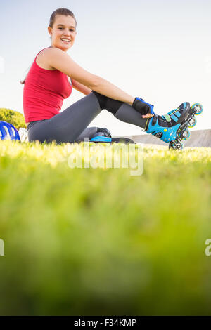 Sorridente sportivo skater bionda seduta in erba Foto Stock