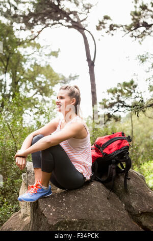 Bionda sorridente escursionista seduta su roccia Foto Stock