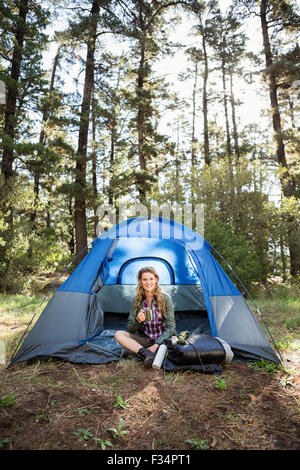 Bella bionda camper sorridente e seduta in tenda Foto Stock