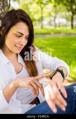 Bella bruna utilizzando smartwatch nel parco Foto Stock