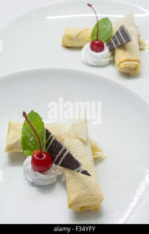 Strudel di mele decorando con crema di farcitura, una ciliegia di colore rosso, un fresco verde foglia di menta, cioccolato sulla piastra bianca su sfondo bianco Foto Stock