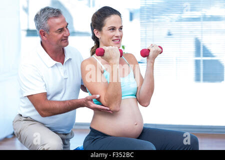 Istruttore assiste la donna incinta nel sollevamento pesi Foto Stock