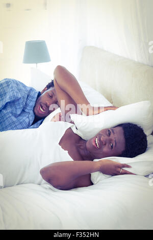 Donna che copre le orecchie con cuscino mentre suo marito è il russamento Foto Stock