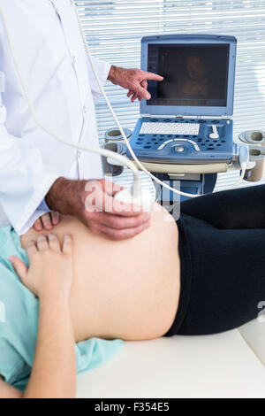 Medico che mostra il monitoraggio a ultrasuoni per donna in stato di gravidanza Foto Stock