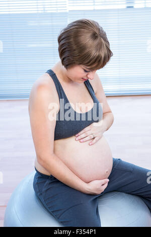 Donna incinta tenendo la pancia mentre è seduto sulla sfera di fitness Foto Stock