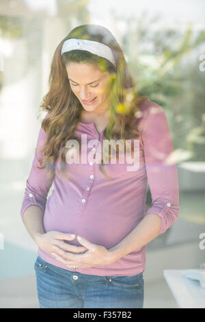 Felice donna incinta in piedi da una finestra Foto Stock