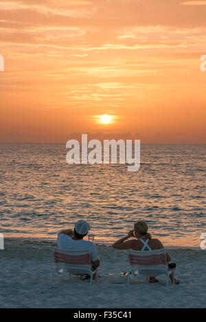 Giovane seduto sulla spiaggia al tramonto, spiaggia di Grace Bay, Providenciales, Turks & Caicos Islands Foto Stock