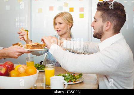 Immagine ritagliata di imprenditore che serve panini ai colleghi Foto Stock