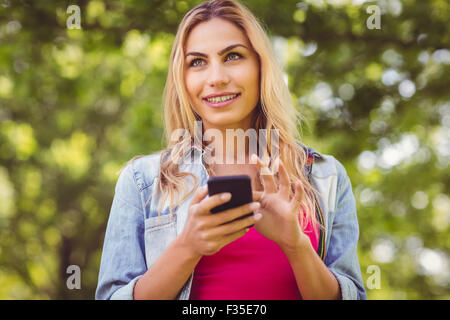 Donna sorridente che guarda lontano mentre si tocca lo smartphone Foto Stock