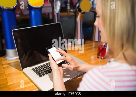 Donna con notebook utilizza lo smartphone a tavola Foto Stock