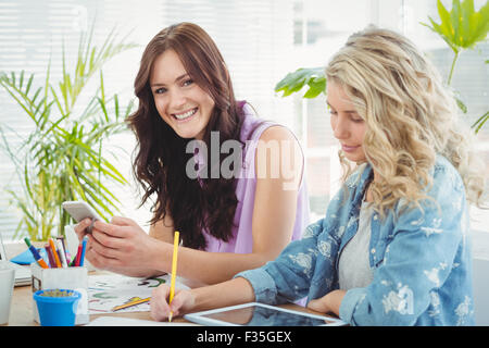 Ritratto di donna sorridente utilizza lo smartphone mentre è seduto alla scrivania Foto Stock