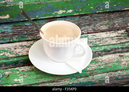 Tazza di caffè con panna è su una vecchia panca di legno in autunno park. Messa a fuoco selettiva con DOF poco profondo Foto Stock