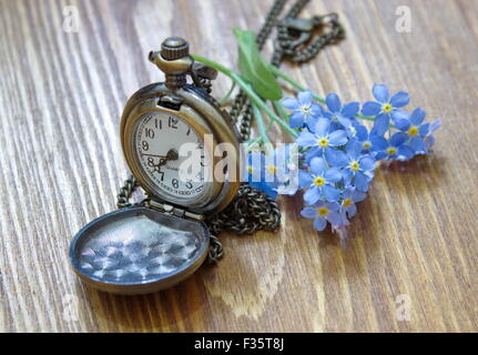 Retrò orologio da tasca con Dimenticare me not giacente sul tavolo di legno Foto Stock