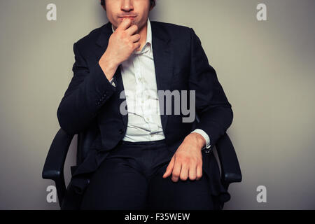 Un oculato imprenditore giovane è seduto in una sedia da ufficio Foto Stock