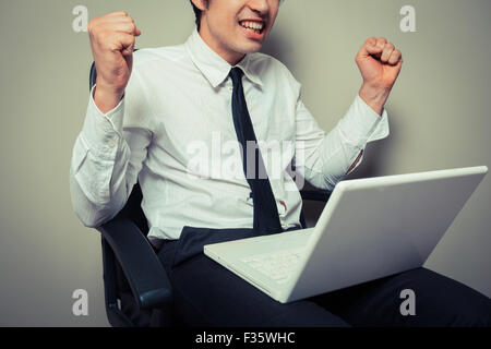 Un giovane imprenditore è seduto in una sedia da ufficio e infiammandosi per il suo computer portatile Foto Stock