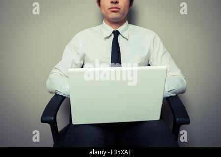 Un giovane imprenditore è seduto in una sedia da ufficio e sta lavorando sul computer portatile Foto Stock