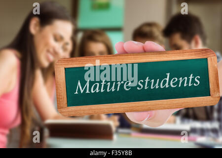 Gli studenti maturi contro sorridente amici seduti a studiare e utilizzando un tablet pc Foto Stock