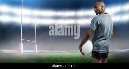 Immagine composita della vista posteriore del fiducioso atleta in piedi con la palla da rugby Foto Stock