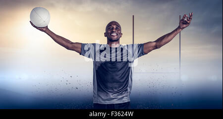 Immagine composita di fiduciosa atleta con bracci sollevati tenendo palla da rugby Foto Stock