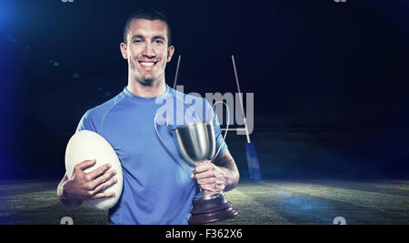 Immagine composita del ritratto di sorridere giocatore di rugby trofeo holding e la sfera Foto Stock