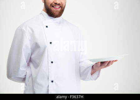 Immagine ritagliata di un maschio felice chef cucinare tenendo la piastra a vuoto isolato su uno sfondo bianco Foto Stock