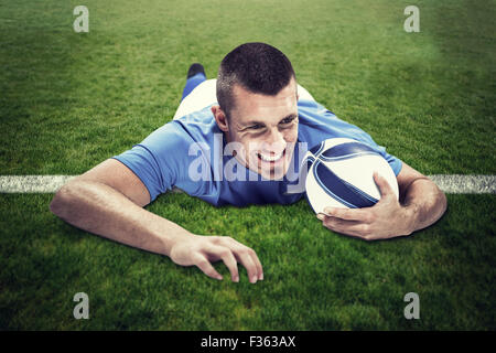 Immagine composita di fiduciosa giocatore di rugby che giace di fronte con sfera Foto Stock