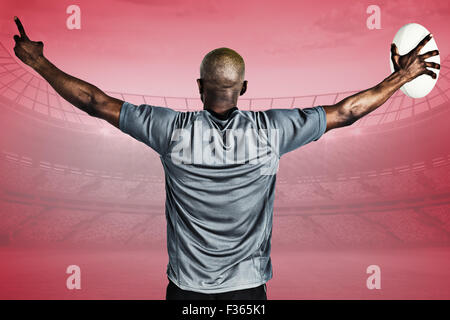 Immagine composita della vista posteriore di uno sportivo con le braccia sollevate tenendo palla da rugby Foto Stock