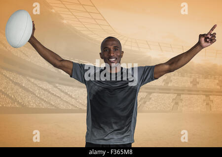 Immagine composita di fiduciosa sportivo con le braccia sollevate tenendo palla da rugby Foto Stock