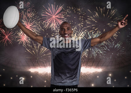 Immagine composita di fiduciosa sportivo con le braccia sollevate tenendo palla da rugby Foto Stock