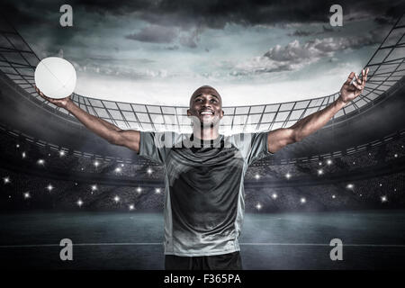 Immagine composita di fiduciosa atleta con bracci sollevati tenendo palla da rugby Foto Stock