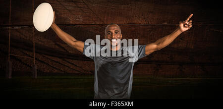 Immagine composita di fiduciosa sportivo con le braccia sollevate tenendo palla da rugby Foto Stock