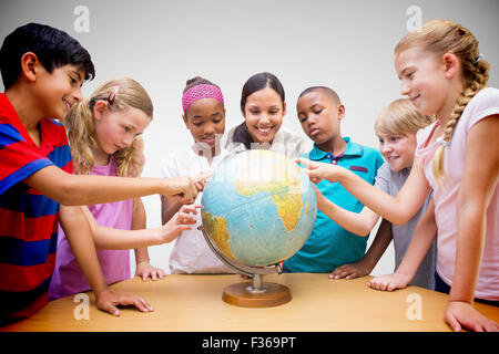 Immagine composita di graziosi gli alunni e gli insegnanti guardando il globo in biblioteca Foto Stock