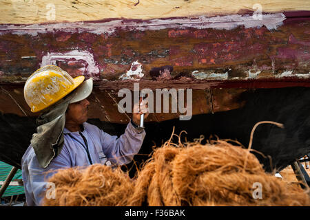 Un lavoratore ecuadoriano impermeabilizzanti in legno tradizionali peschereccio in un cantiere navale a Manta, Ecuador. Foto Stock