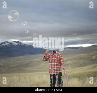 Testa di uomo a soffiare bolle montagne cielo tempestoso Foto Stock