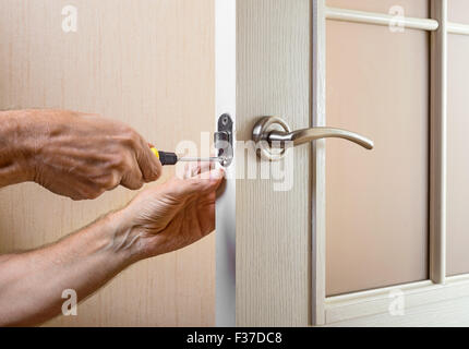 Un uomo è il montaggio della protezione sciopero del catenaccio su una porta di vetro con un moderno stile curvo con impugnatura in nichel utilizzando un screwdr Foto Stock