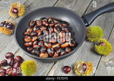 Saporite castagne arrostite in una padella su di un tavolo di legno Foto Stock