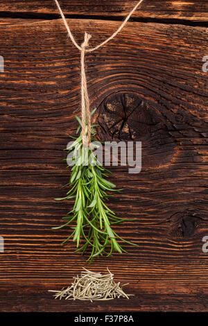 Fresco e rosmarino secco cantato sul legno rustico sfondo. Delizie di erbe aromatiche. Foto Stock