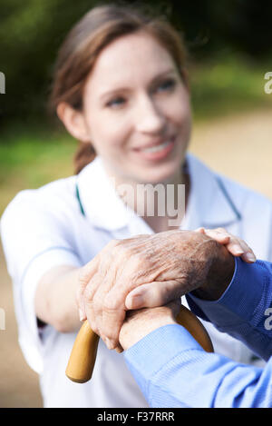 Senior dell'uomo mani appoggiate sul bastone con cura lavoratore in background Foto Stock