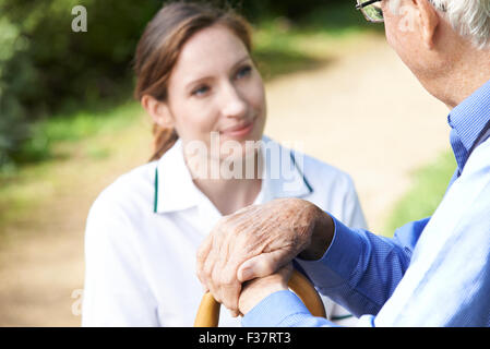 Senior dell'uomo mani appoggiate sul bastone con cura lavoratore in background Foto Stock